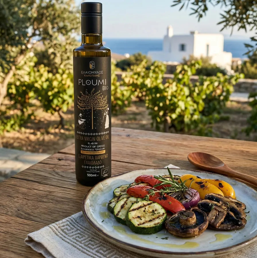 PLOUMI BIO organic extra virgin olive oil 500ml bottle on an outdoor table with a plate of grilled vegetables, olive grove and sea view in the background — Karepidis Estate